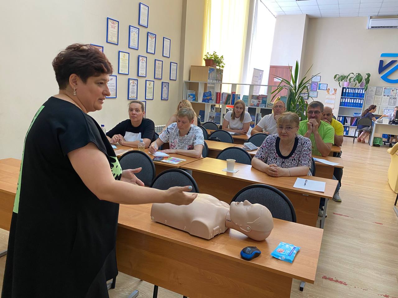 Занятие по первой помощи в учебном центре «Вертикаль»: преподаватель объясняет группе приёмы реанимации, на столе манекен